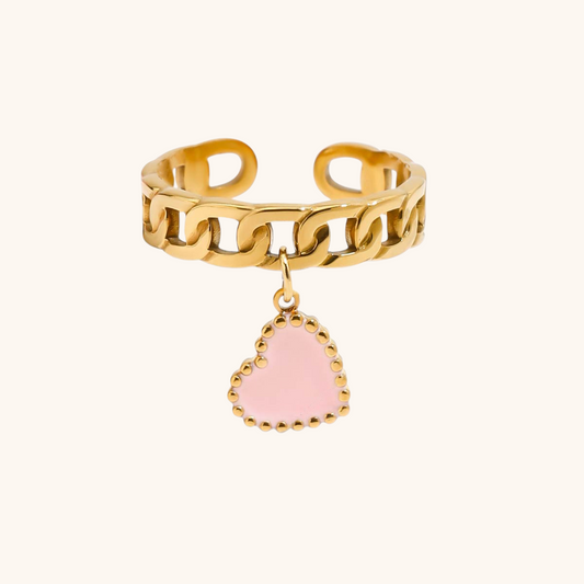 Close-up of pink enamel heart charm ring styled on hand with layered jewelry