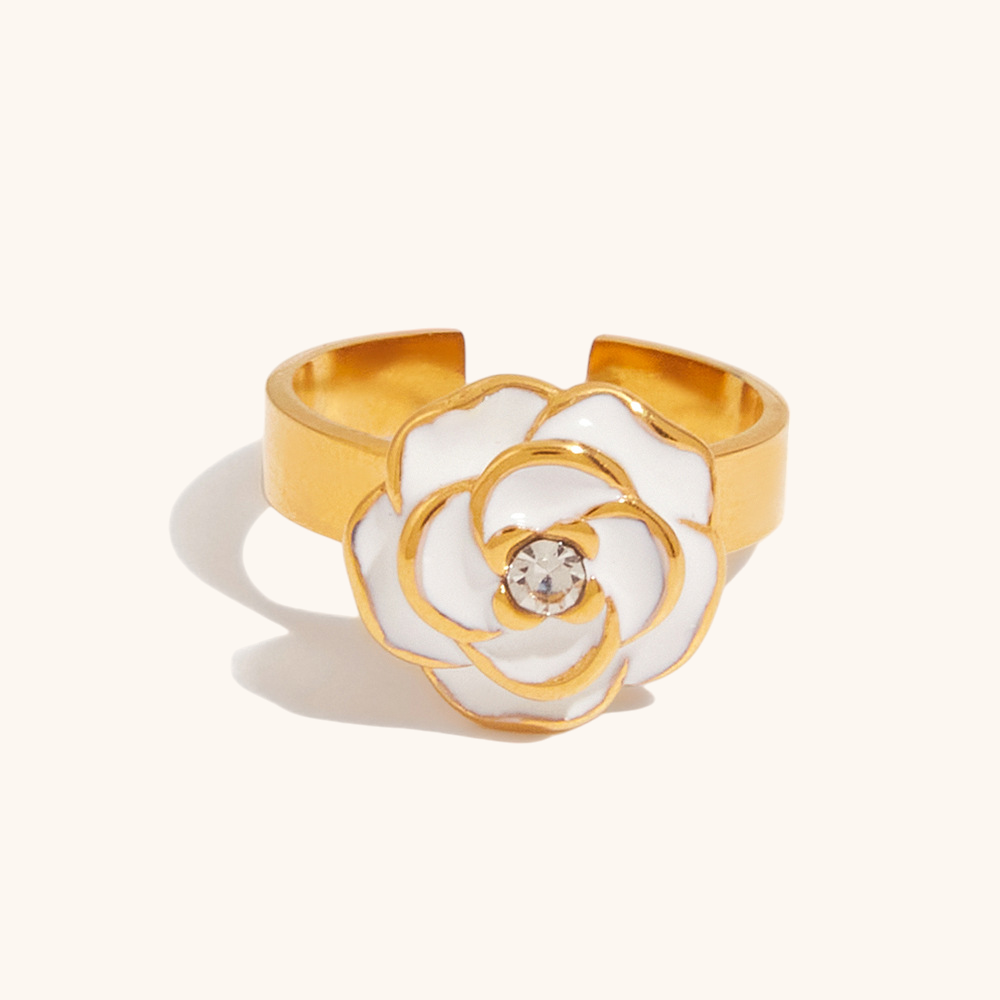 Front-facing product image of a gold-tone open ring featuring a sculpted white enamel flower