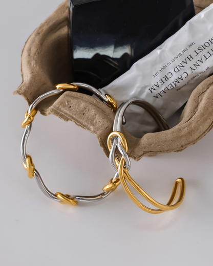 Gold and silver hoop earrings on a textured surface with a black container and white paper in the background.