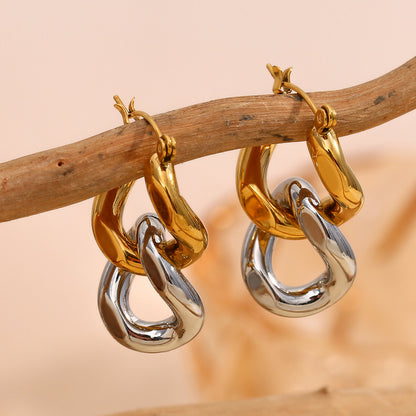 Chunky gold and silver hoop earrings hanging from a wooden branch for natural styling
