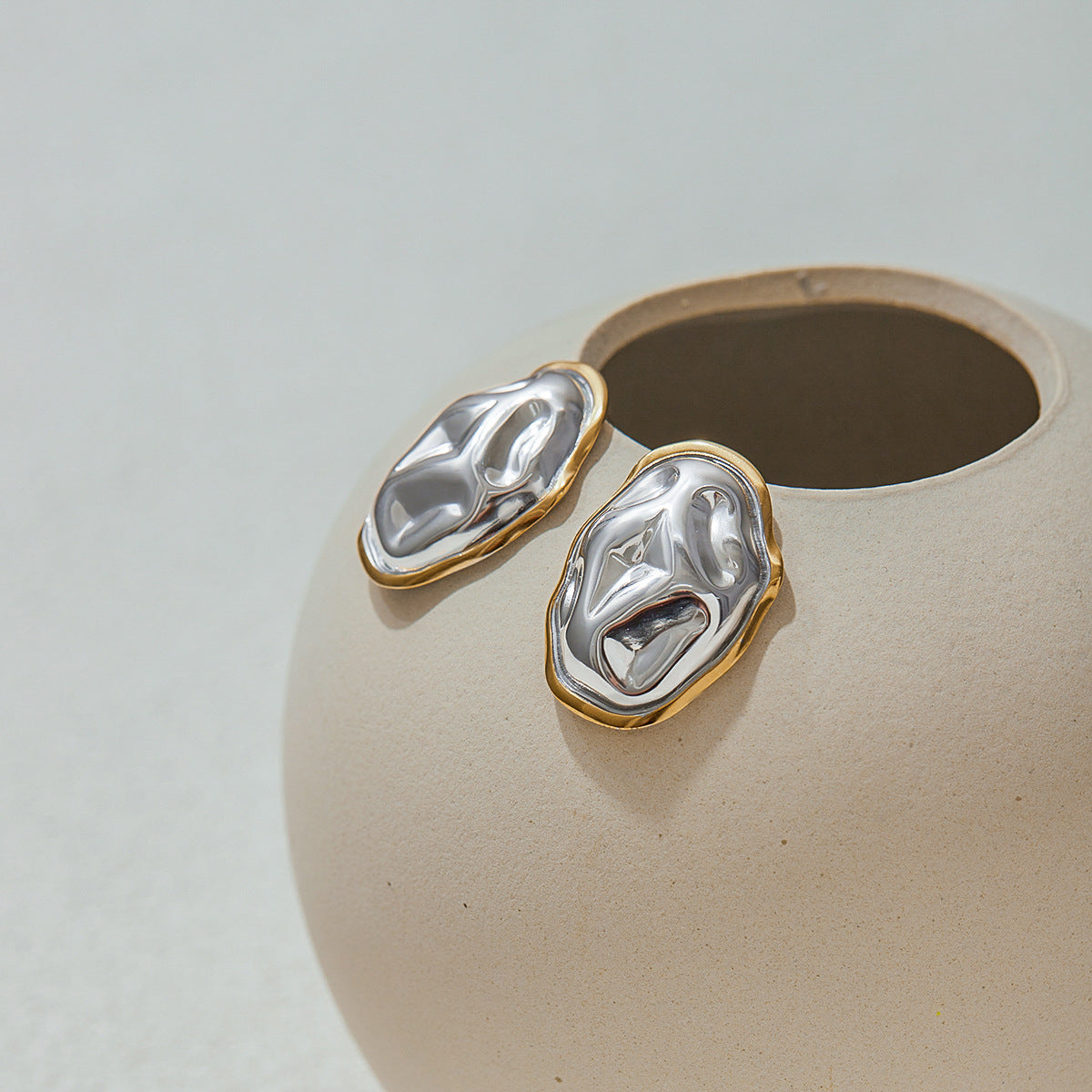 bold sculptural metal earrings with fluid form, laid on beige vase, ideal for statement jewelry lovers