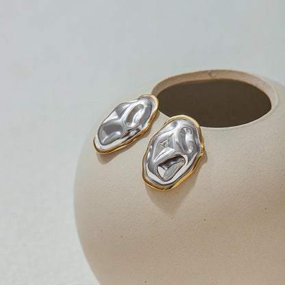bold sculptural metal earrings with fluid form, laid on beige vase, ideal for statement jewelry lovers