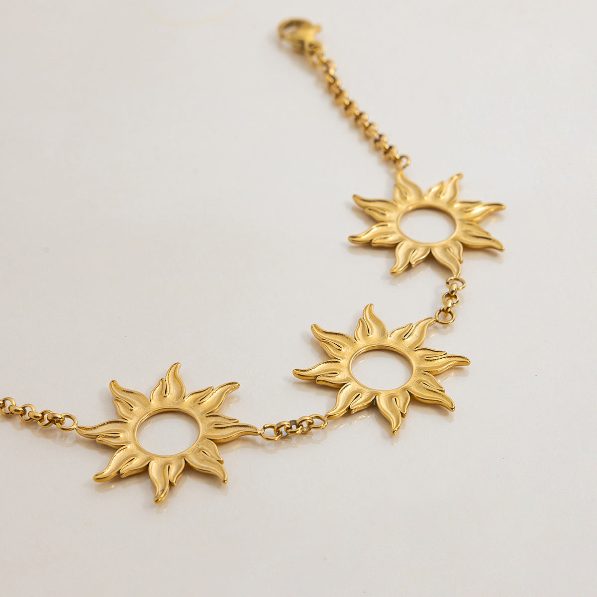 Studio shot of the back of a gold bracelet with three sun-shaped pendants on a cream background