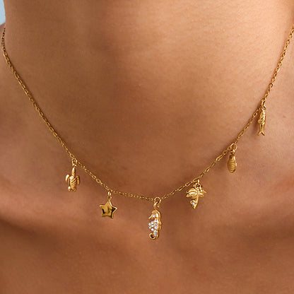 Model wears gold beach charm necklace with sea turtle, seahorse, and star charms on collarbone