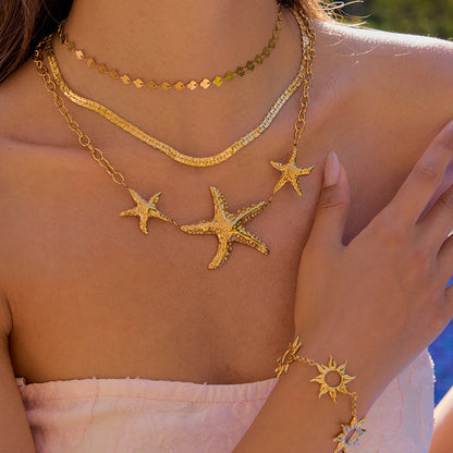 Golden starfish necklace styled on female model's neck with poolside sunlight, layered with minimalist chokers