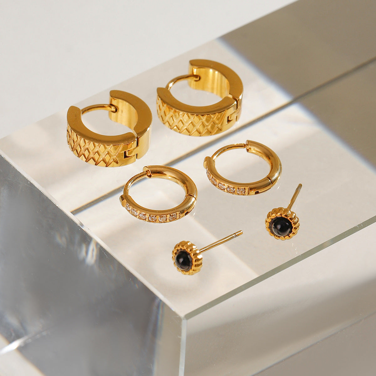 A jewelry flat lay with black gemstone studs and gold huggie hoops accented with cubic zirconia.
