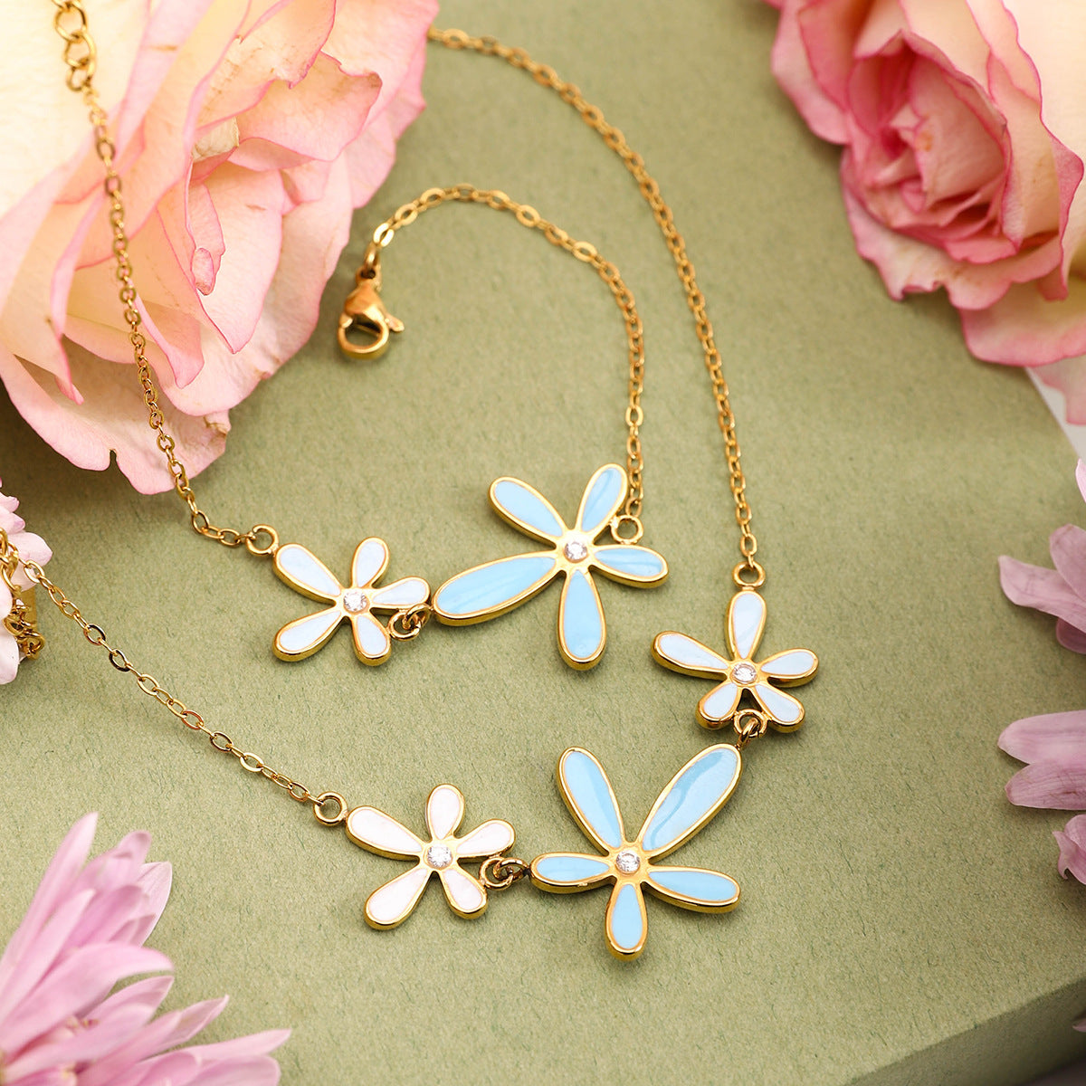 Layered enamel flower bracelet and necklace set displayed on green background with roses