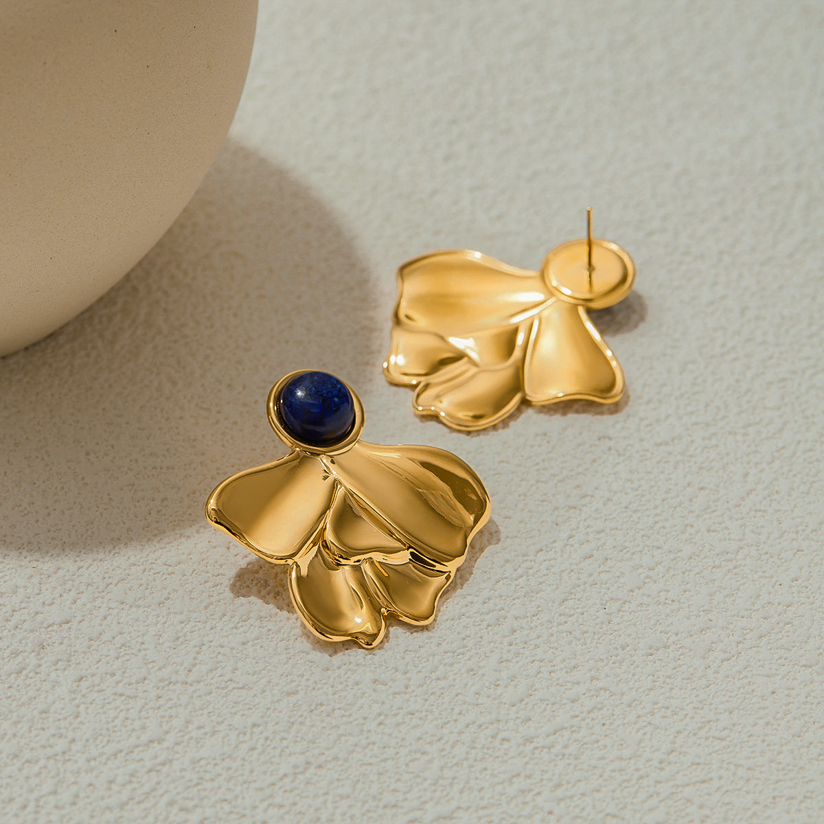Sculptural gold floral earrings on textured surface