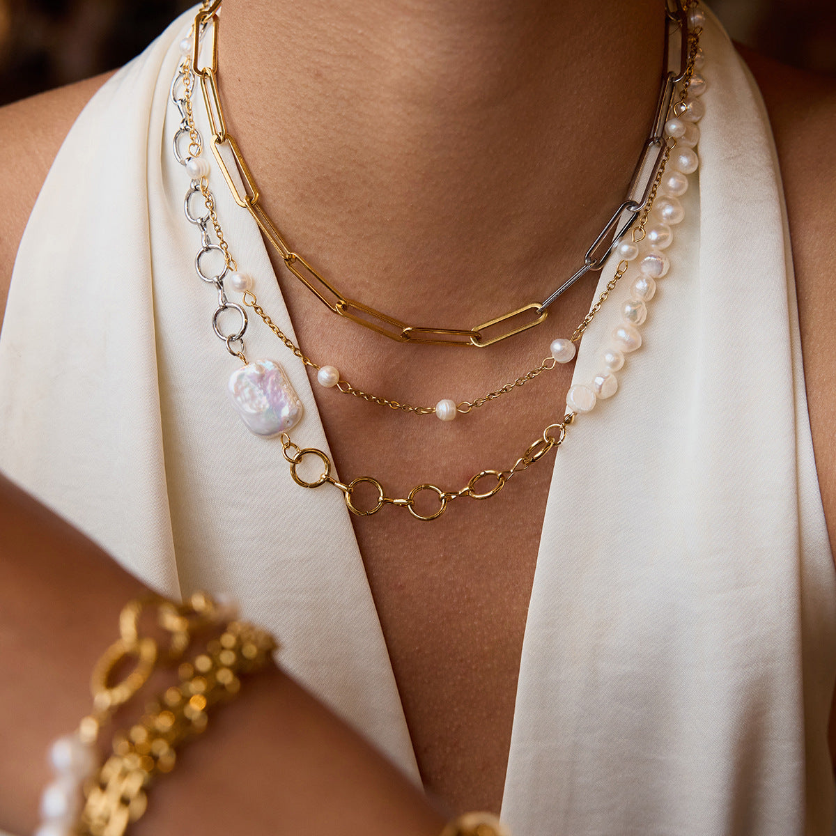 Close-up of stacked pearl and gold necklaces styled on a woman in an ivory blouse