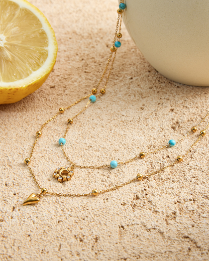 Gold necklace with blue beads on a textured surface with a lemon and white object in the background