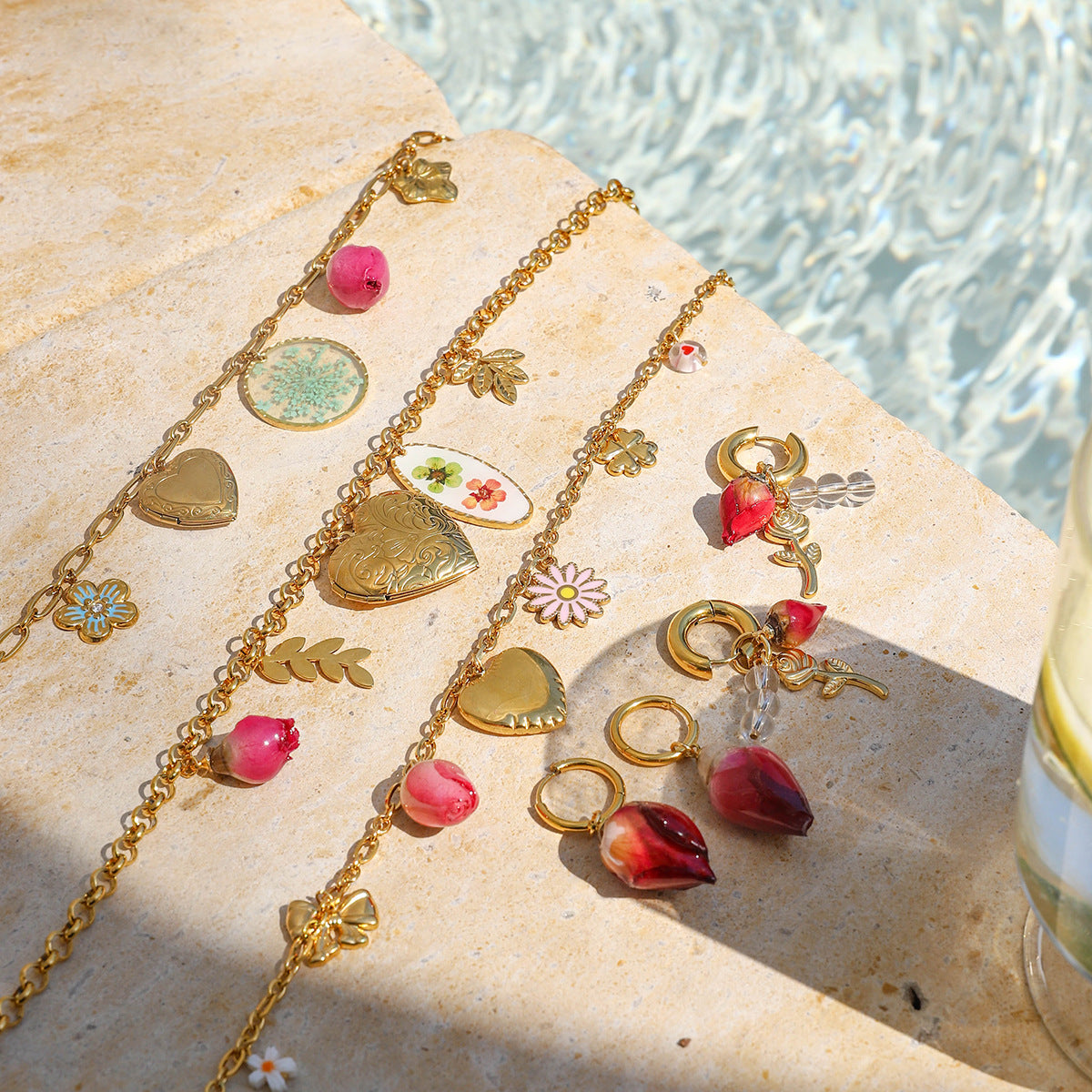 Summer-inspired floral and heart charm necklaces arranged under sunlight near a pool