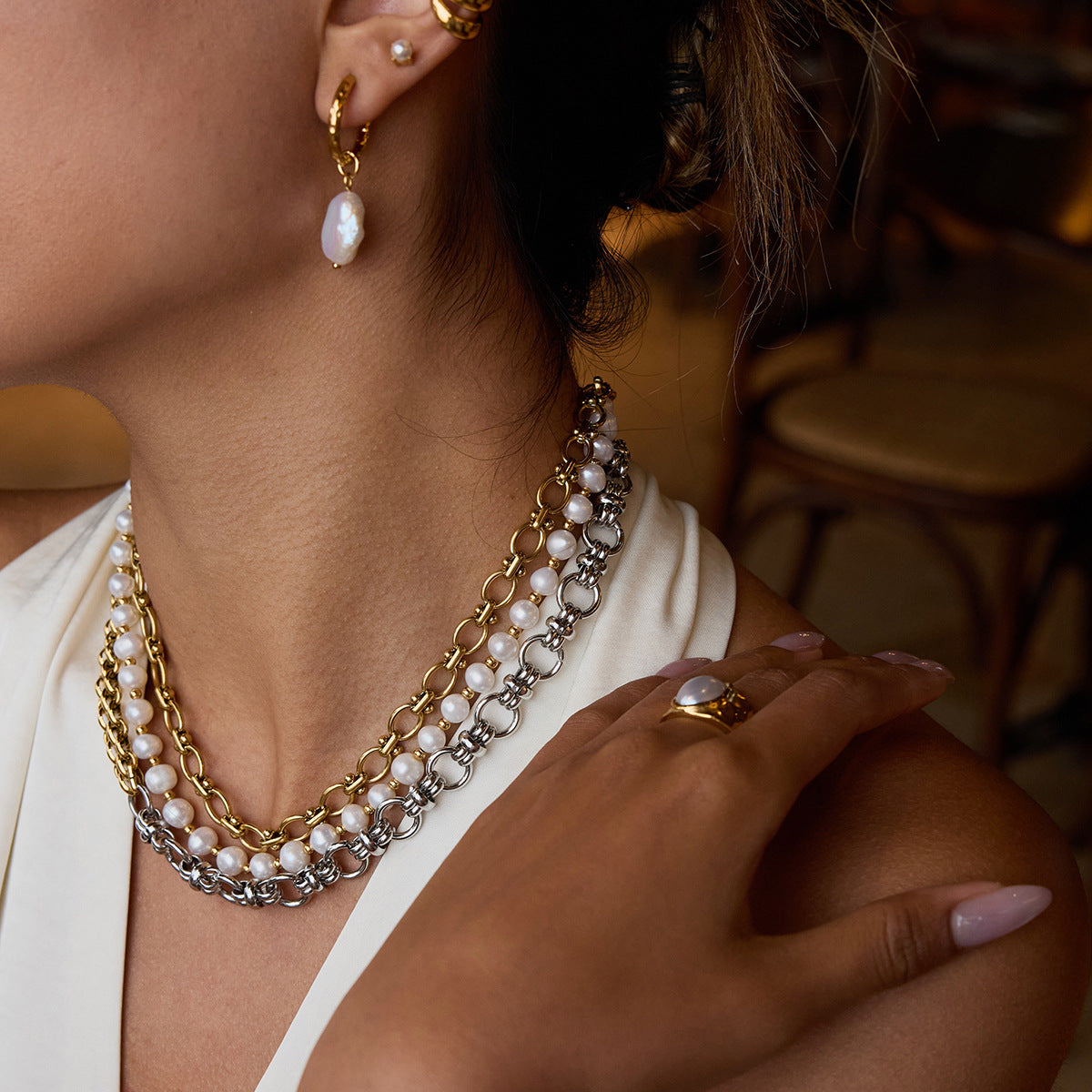 Two-tone gold and silver chain necklace worn with a deep V white top, showing bold layering and pearl accents.