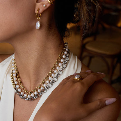 Two-tone gold and silver chain necklace worn with a deep V white top, showing bold layering and pearl accents.