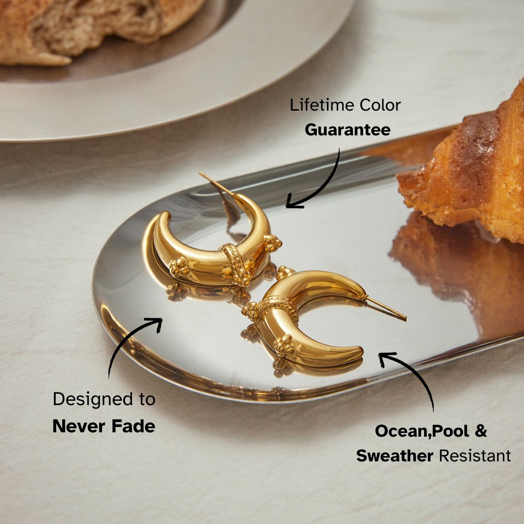 Crescent-shaped gold hoop earrings with ornate beaded detailing on reflective tray