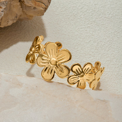 Close-up of a sculpted floral gold cuff bracelet on a light stone background
