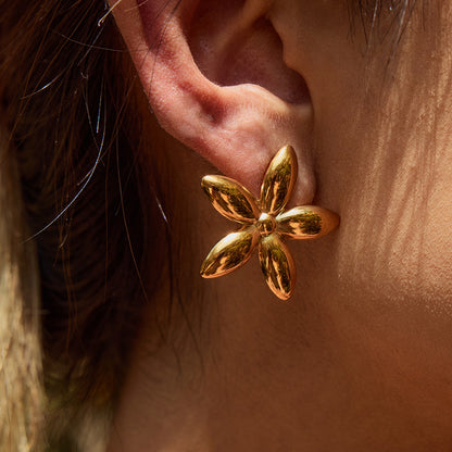 Close-up of bold gold flower-shaped earrings worn outdoors