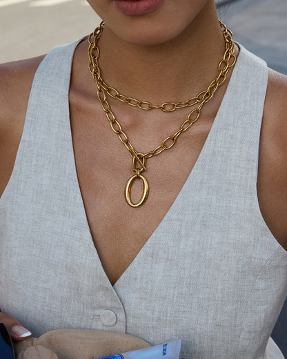 Person wearing a gold chain necklace with a pendant, dressed in a light gray sleeveless top.