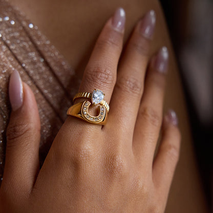 Model hand wearing the gold horseshoe ring paired with a pear-cut ring in a sparkly outfit