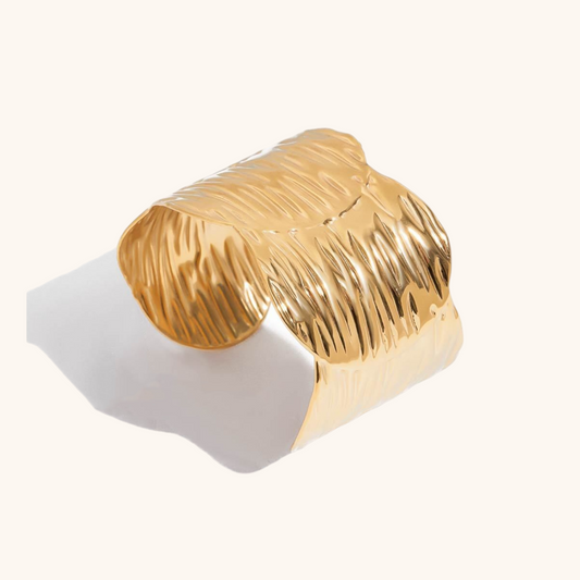 Studio close-up of a sculptural wide cuff bracelet with wave-inspired gold texture and a high-polish finish.