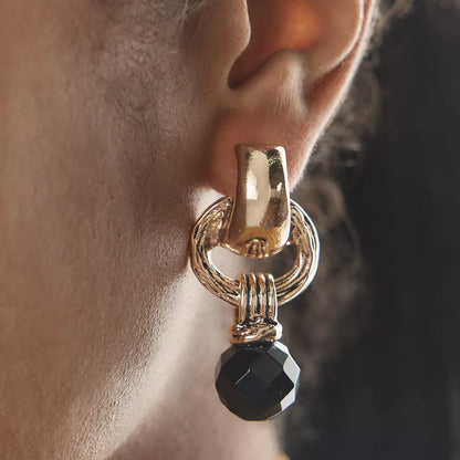 Model wearing bold gold and black drop earrings with sleek hairstyle