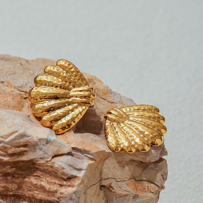 Close-up of textured gold shell earrings on natural rock background