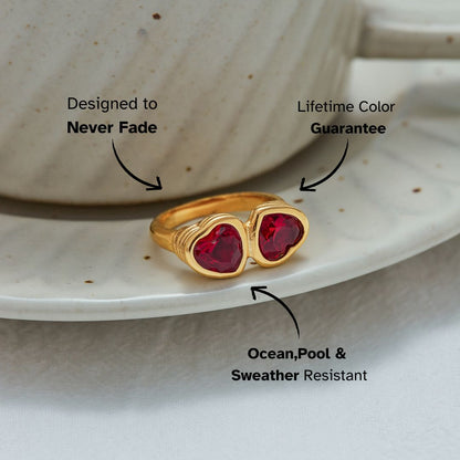 Gold open band ring with double red heart-shaped gemstones on a ceramic plate