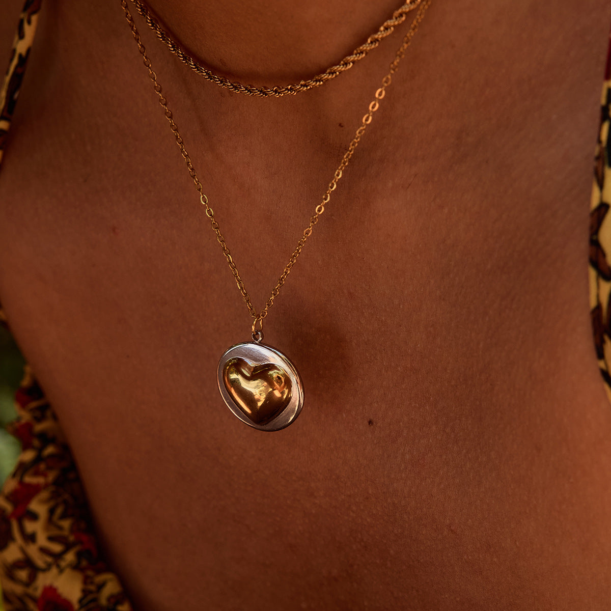 Model wearing a two-tone heart pendant necklace layered with gold chain, beachwear outfit