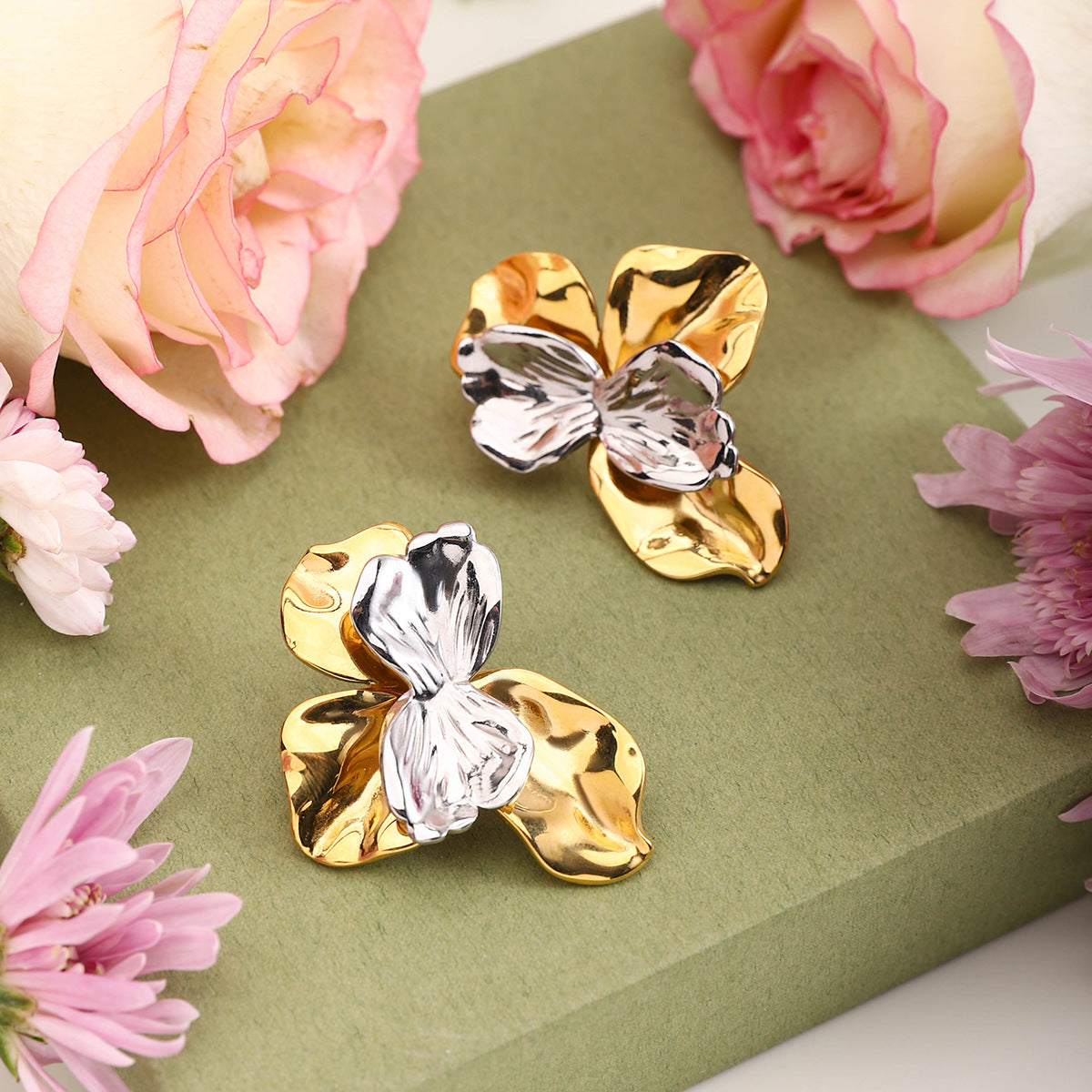 Artistic flower earrings placed beside roses on soft green background