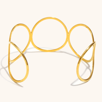 Sculptural gold metal cuff bracelet with open loops and negative space design, artistic layout shot.