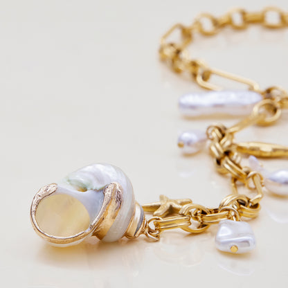 Gold chain bracelet with pearl charms on a light background