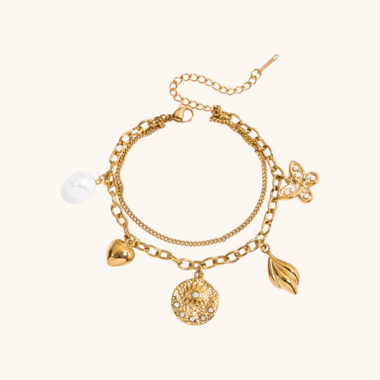 Gold charm bracelet featuring butterfly, evil eye, and pearl pendants on beige background