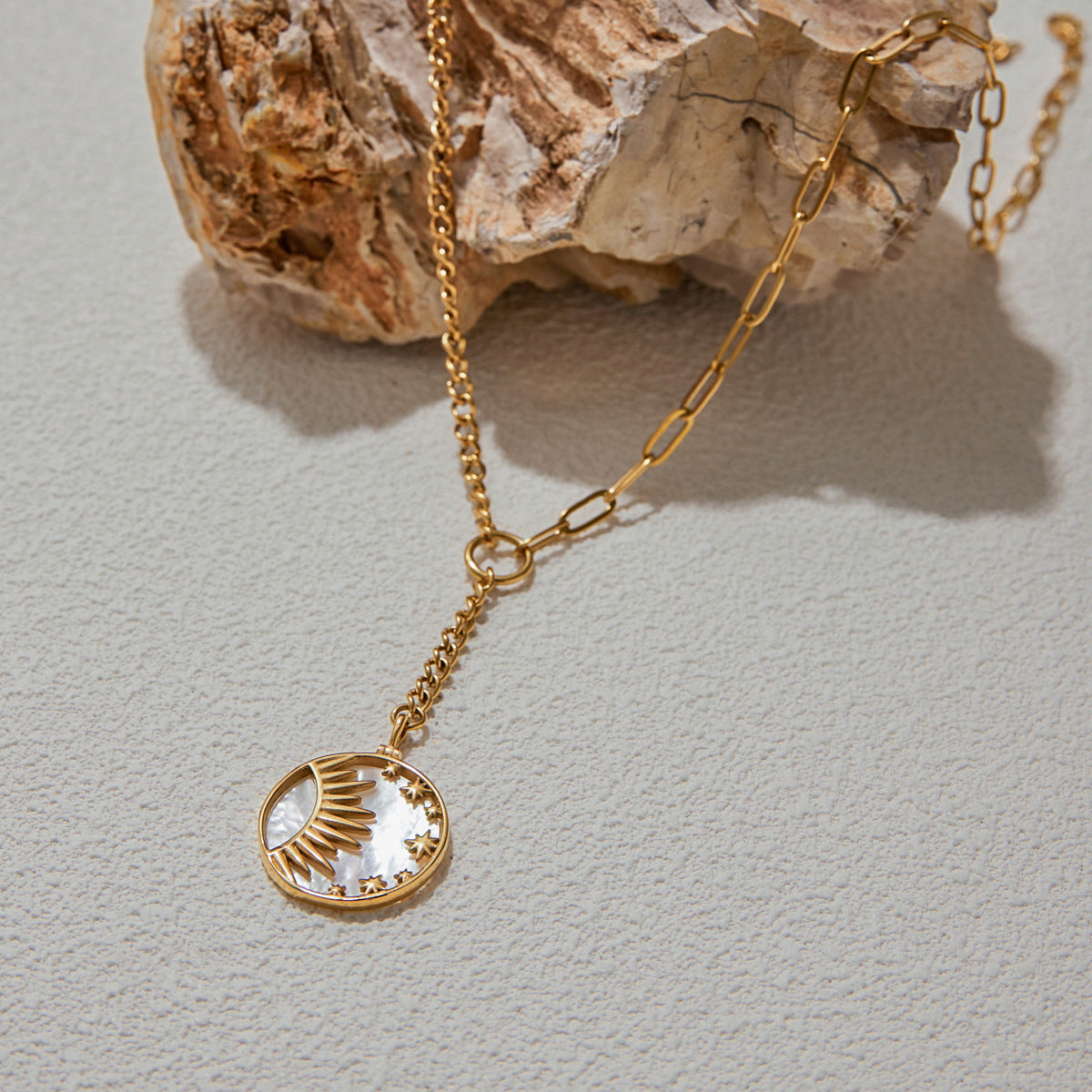 Mother-of-pearl pendant necklace styled with gold chain and texture backdrop