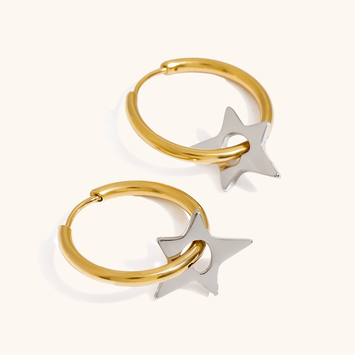 Gold hoop earrings with silver star pendants, flat-lay on white background