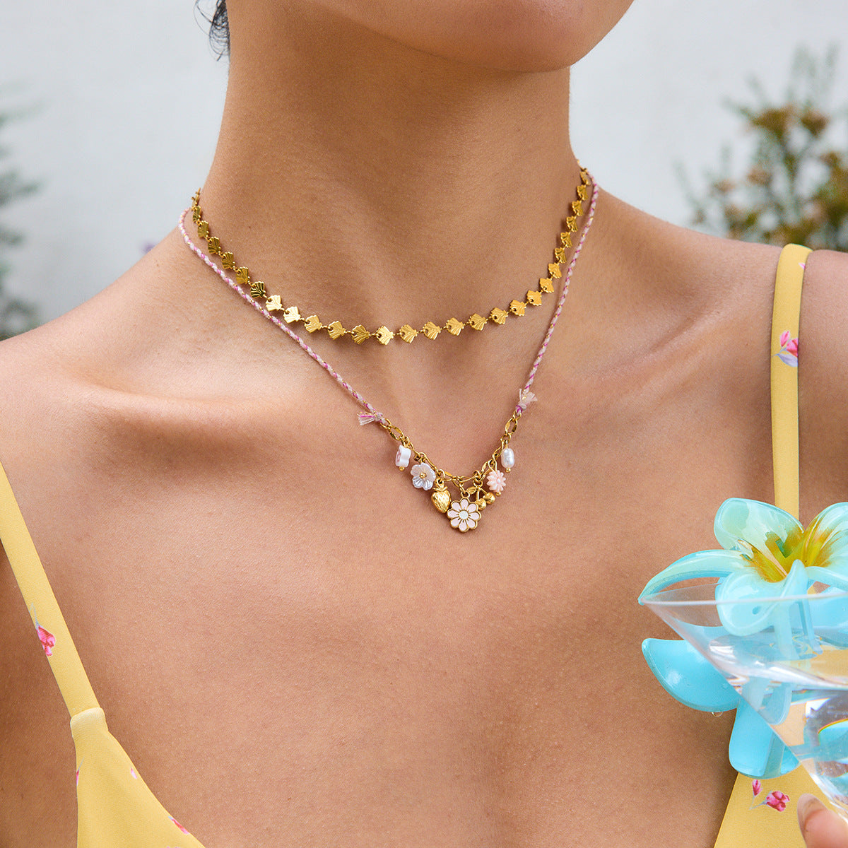 Model wearing layered gold and pink charm necklace in a summery floral outfit