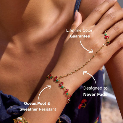 Close-up of a model wearing a cherry-themed hand chain with ring under sunlight by the beach