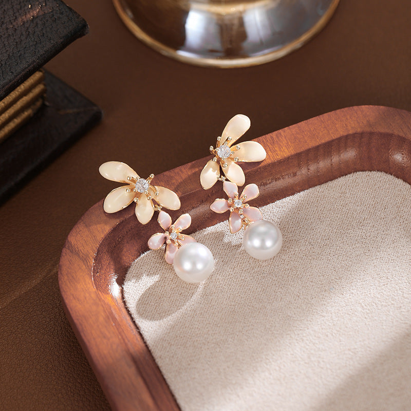 Chic pearl and pink flower earrings with sparkling gem centers, showcased in a jewelry plate against a cozy indoor background.