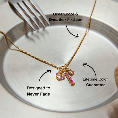 Close-up of gold necklace with pink crystal heart charm lying on a silver plate