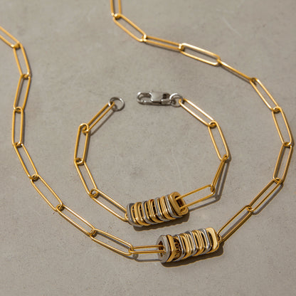 Close-up of chunky gold and silver necklace and bracelet on neutral background, emphasizing bold fashion details.