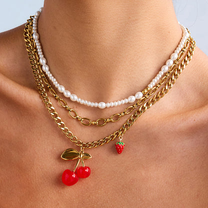 Close-up of gold cherry charm necklace layered with pearls on a woman’s neck