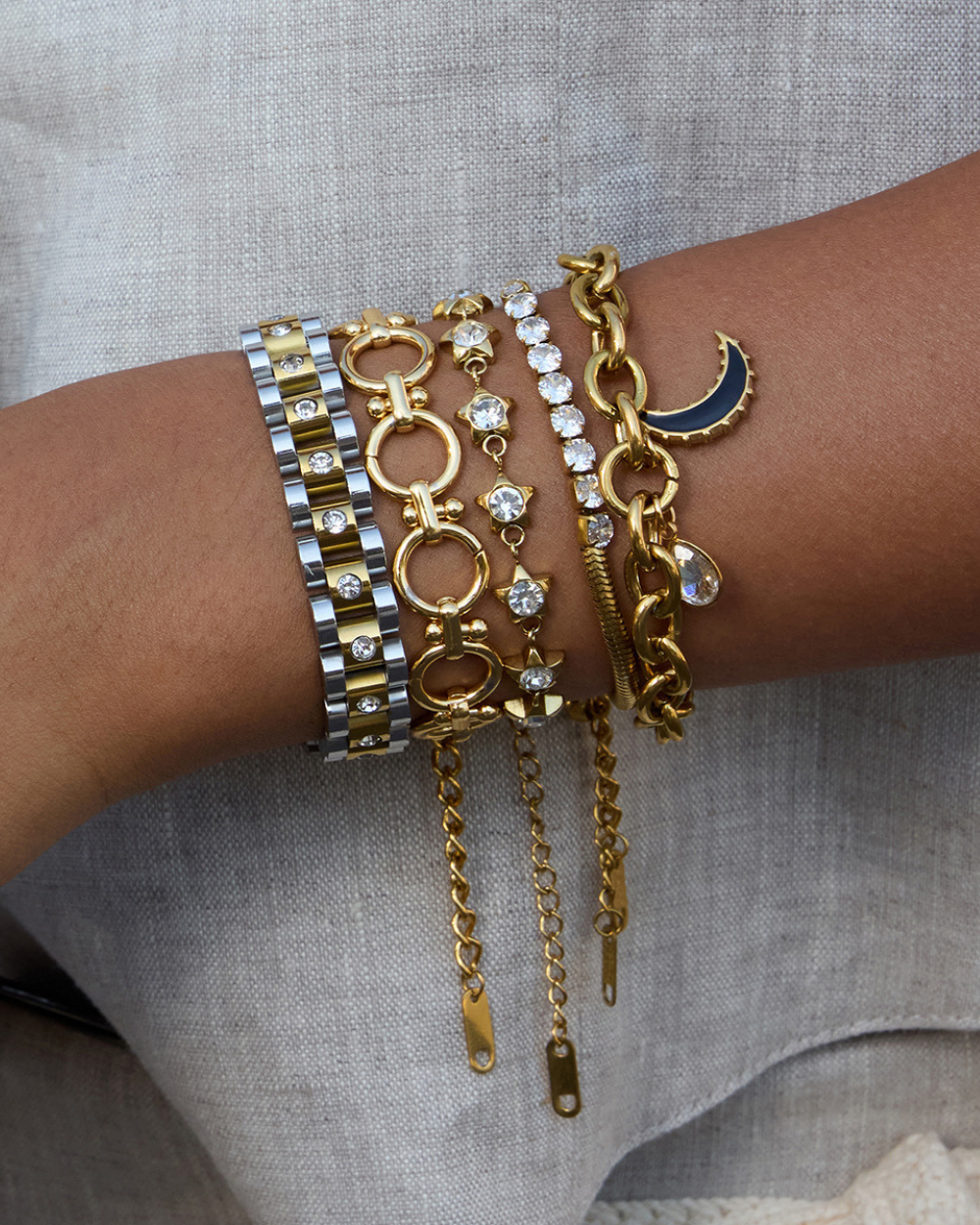 Multiple gold and silver bracelets on a wrist against a neutral background