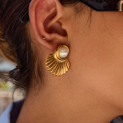 Model showcasing gold shell stud earrings with sunglasses and blue blouse.