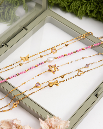 Set of gold and pink beaded necklaces with star, heart, and bow charms in a display case.