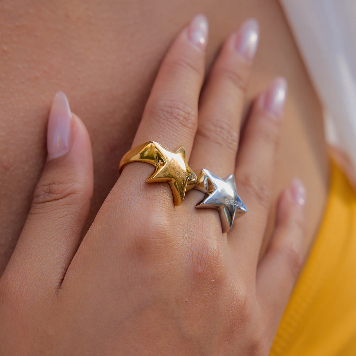 Close-up of hand with two bold star rings worn together on fingers