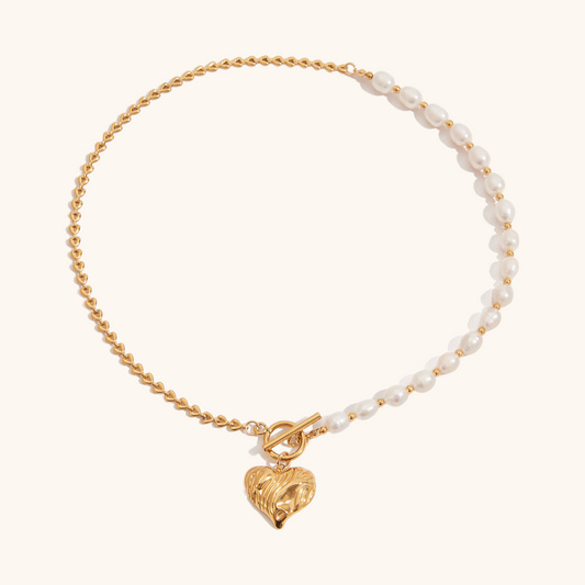 Detailed view of gold heart-shaped pendant paired with freshwater pearls and gold chain on a white surface