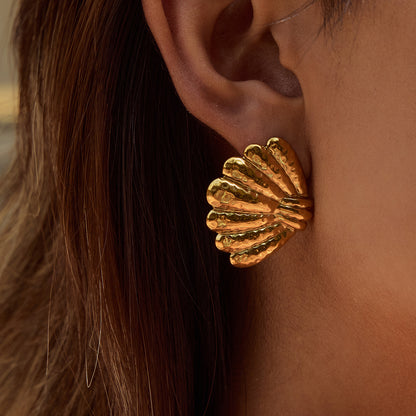 Model showcasing large gold seashell earrings with hair tucked back