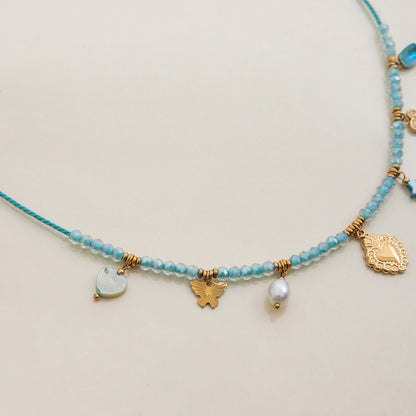side view of beaded necklace with layered gold charms and blue crystal pendant