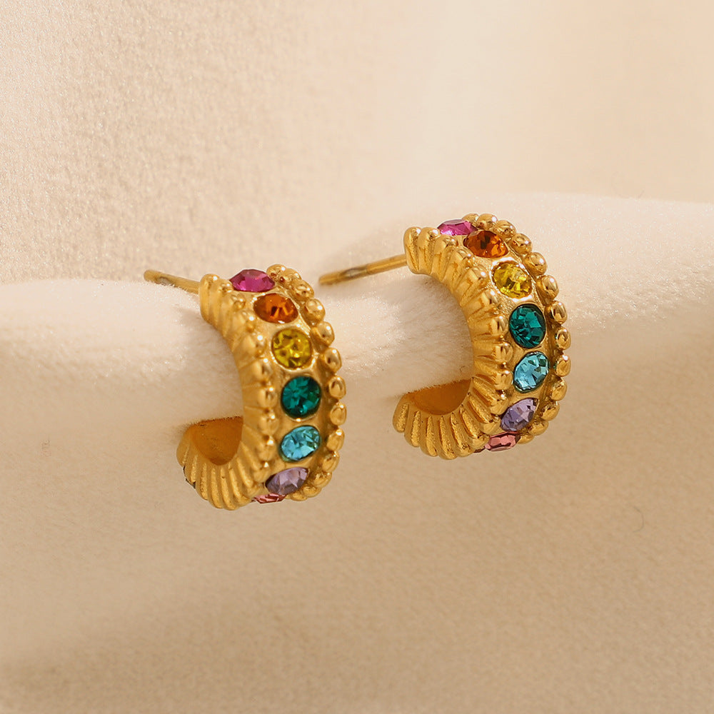 Gold rainbow hoop earrings with colorful gemstones on a soft fabric display
