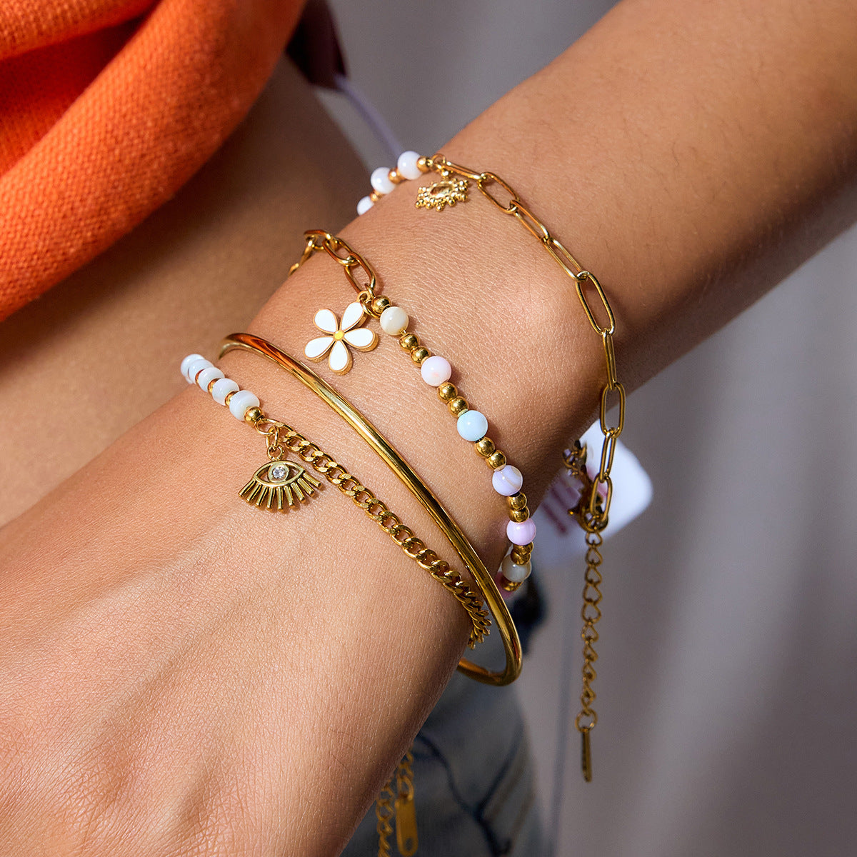 Close-up of a wrist wearing multiple gold bracelets with various charms on a blurred background.