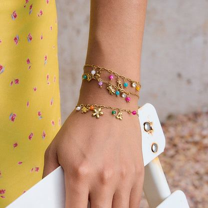 Model wearing layered gold bracelets with colorful charms outdoors