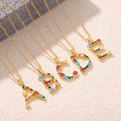 Colorful alphabet pendant necklaces featuring zircon stones in red, blue, green, and yellow, showcasing letters A, B, C, D, and E on a golden chain with a textured background.